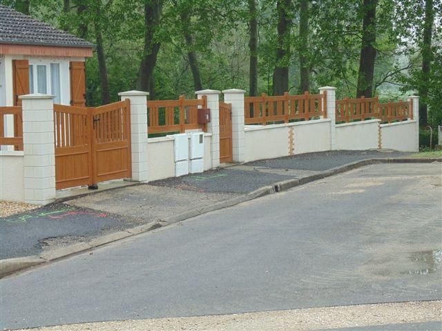 Rue résidentielle avec une clôture blanche, un portail en bois et des arbres le long d'une route sinueuse