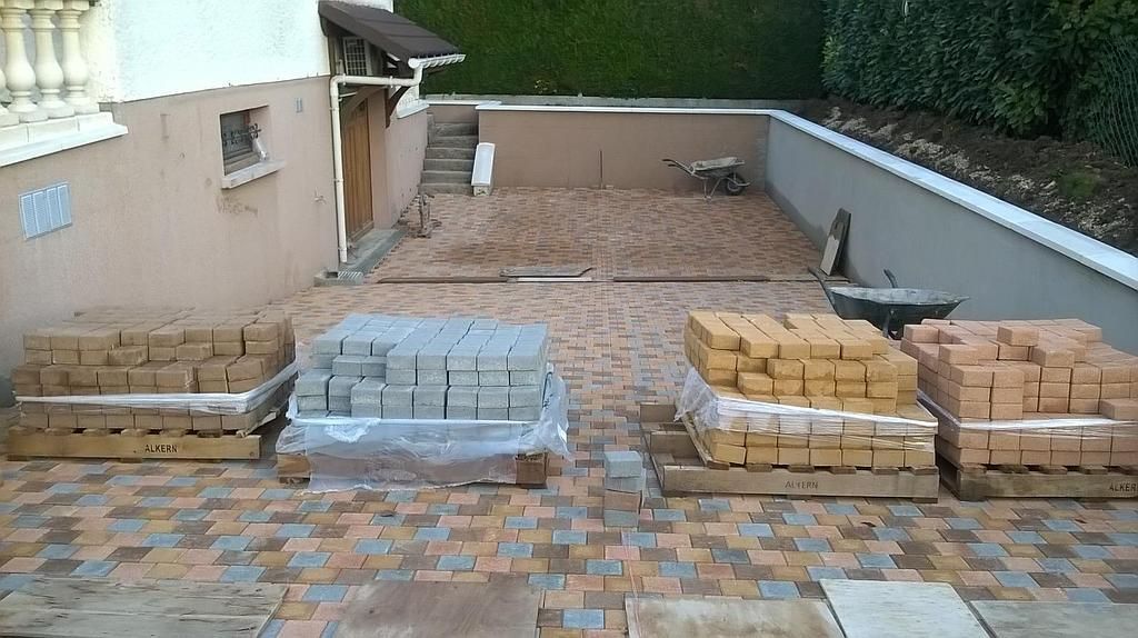 Des piles de pavés et de briques disposées dans une terrasse à l'arrière d'une maison.
