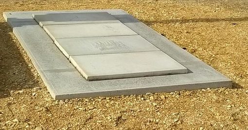 Une petite dalle de béton avec une trappe métallique rectangulaire posée sur du gravier.