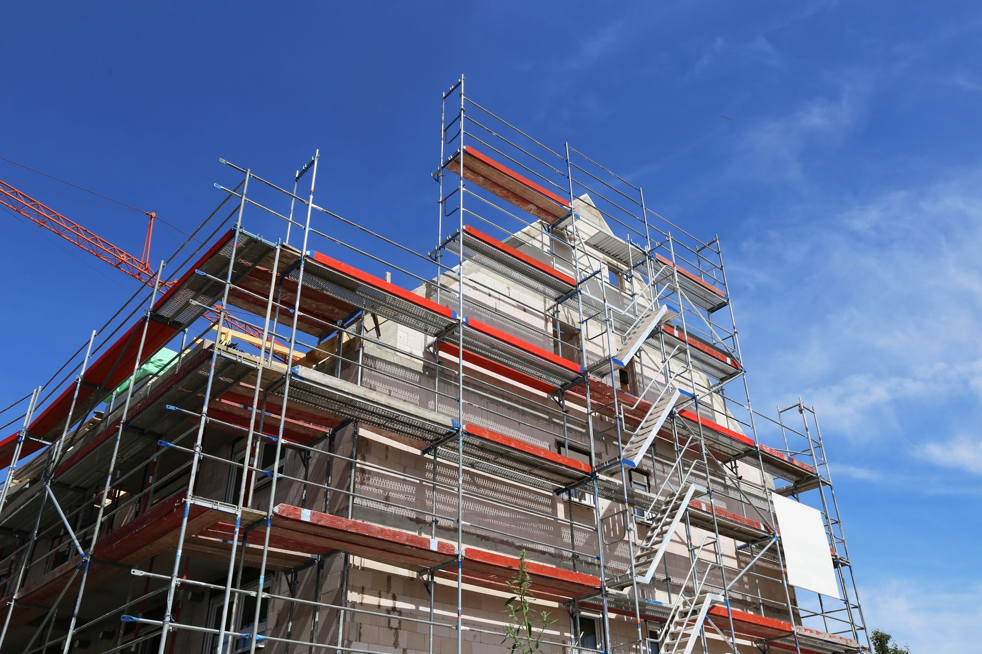 Vue en contre-plongée d'un immeuble de plusieurs étages en construction, entouré d'échafaudages orange et métalliques sur fond de ciel bleu.