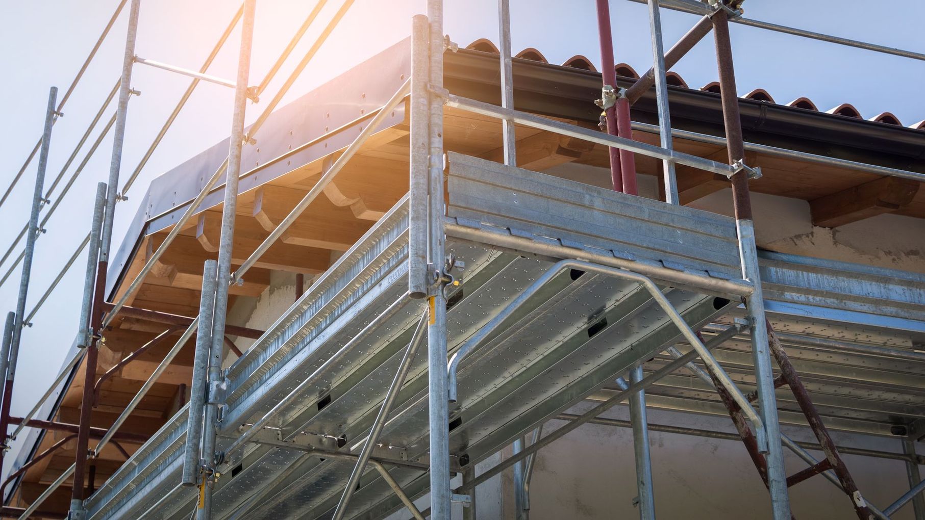 Des échafaudages métalliques entourent le toit d'un bâtiment en construction, illuminé par la vive lumière du soleil.