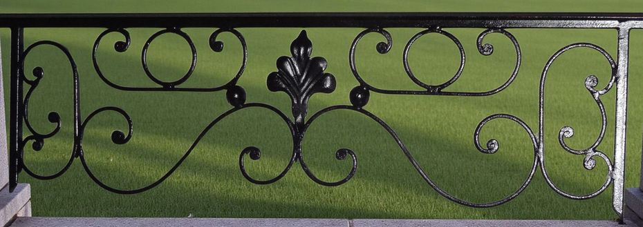 Rambarde en fer forgé noir ornée de volutes décoratives, sur fond d'herbe verte.