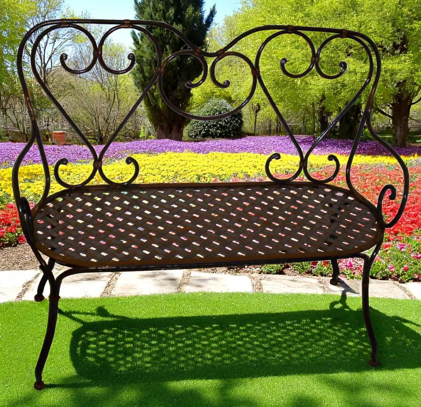 Un banc en fer forgé avec des formes de cœur devant un parterre de fleurs