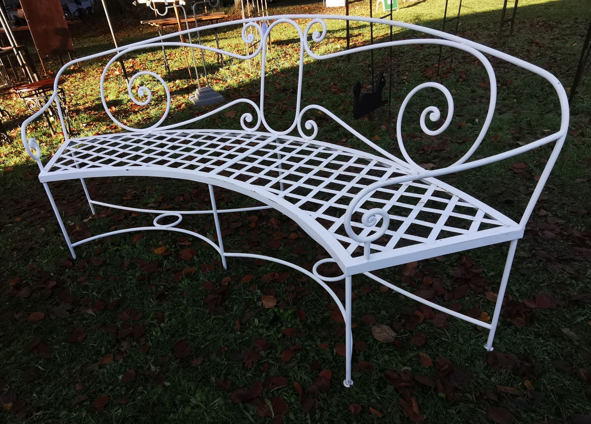 Banc suspendu en fer forgé avec auvent, sur un chemin de pierre dans un jardin.