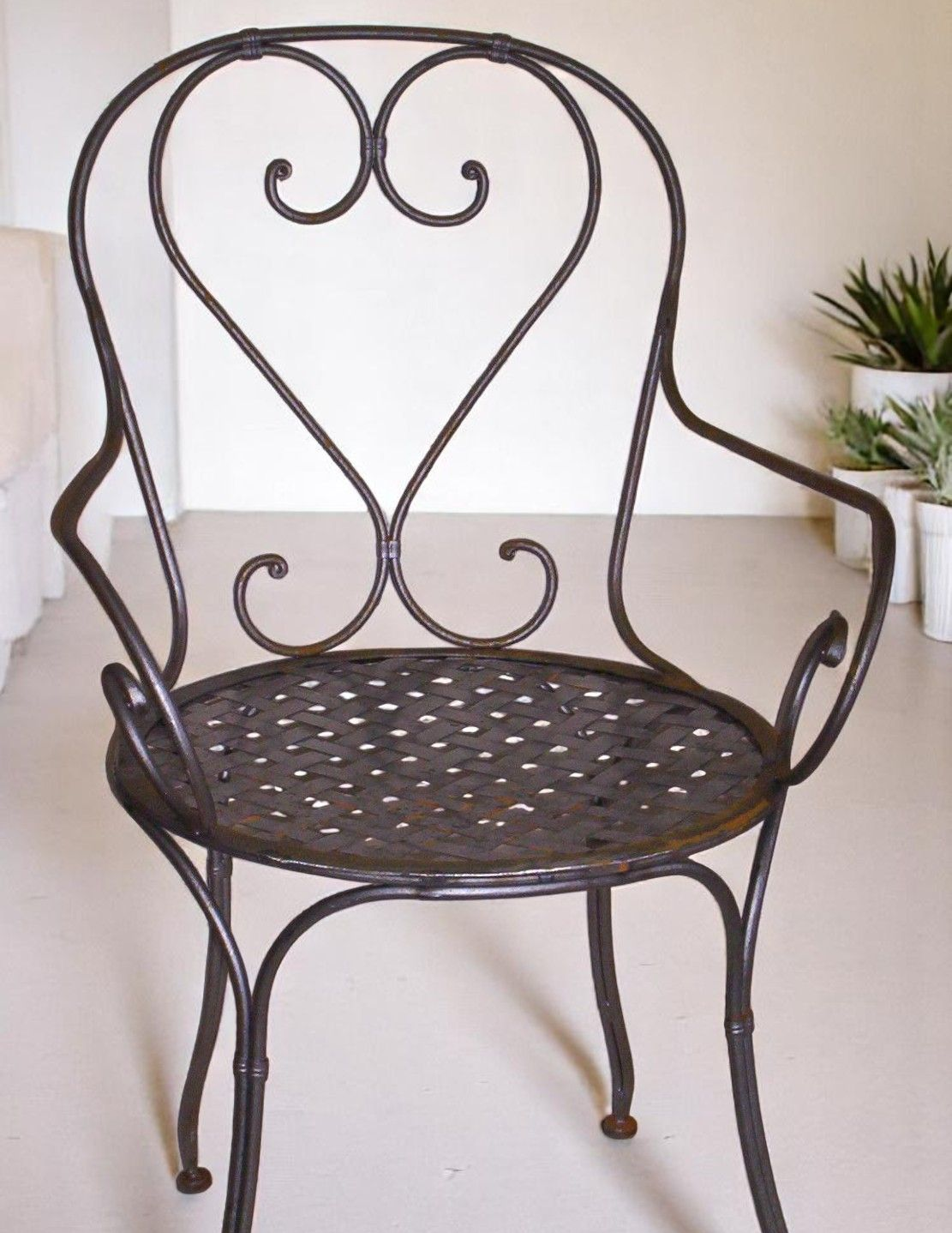 Chaise d'intérieur en fer forgé noir, avec dossier en forme de cœur et assise perforée.
