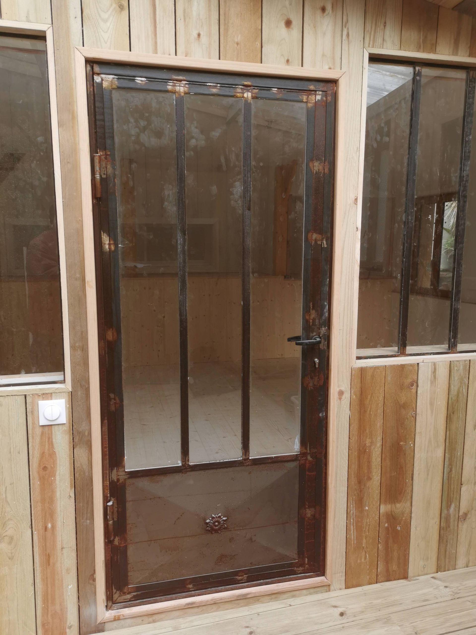 Porte à cadre métallique avec panneau transparent, entourée de murs en bois.