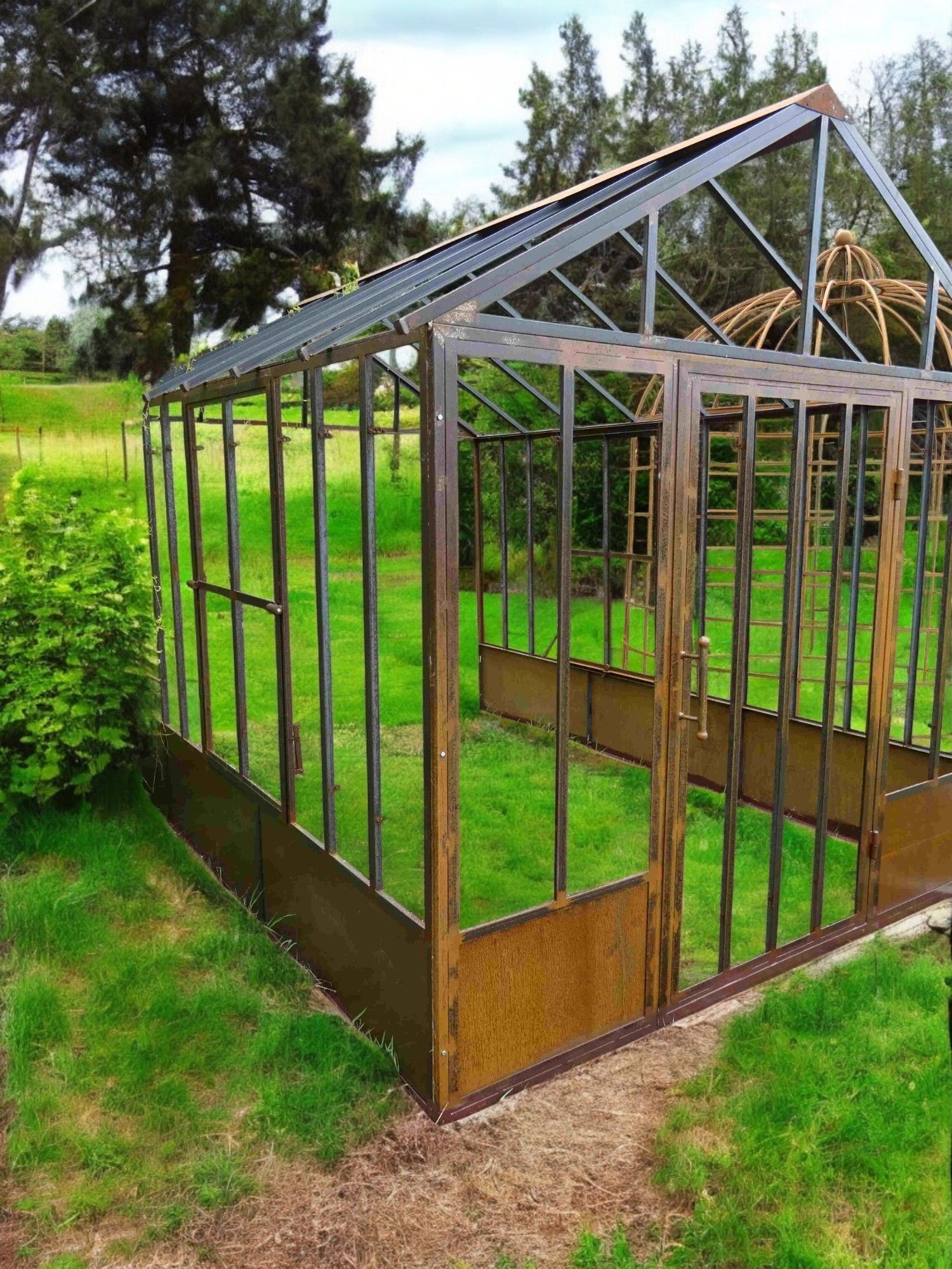 Serre à structure métallique et parois de verre, installée dans un jardin gazonné.