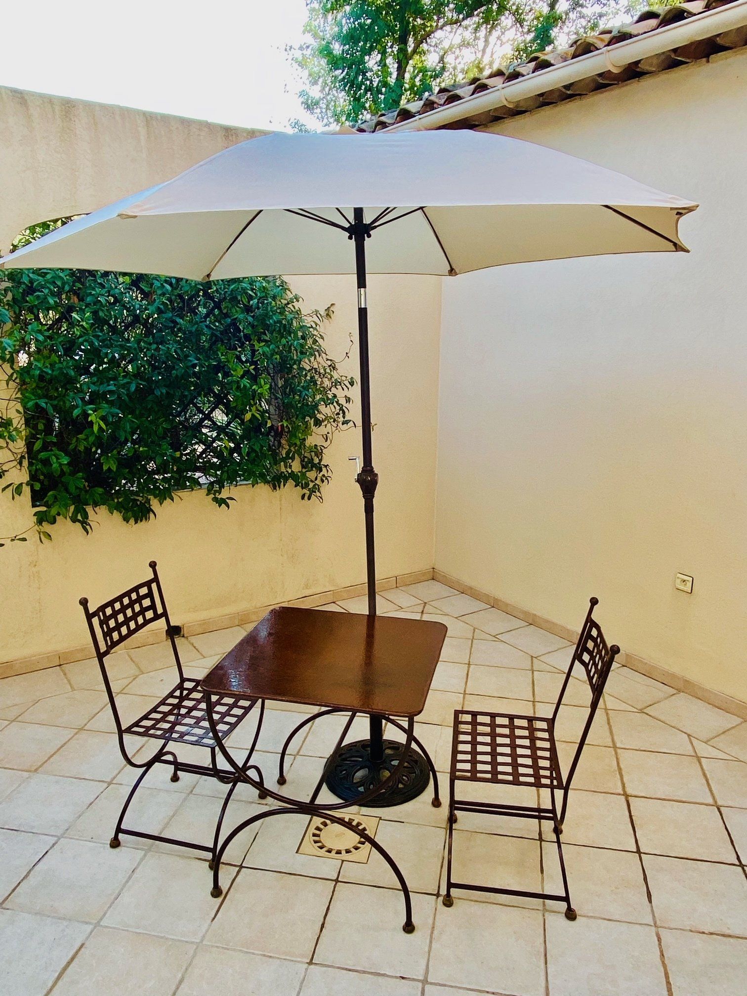 Ensemble de patio comprenant une table, deux chaises et un parasol sur une terrasse carrelée.