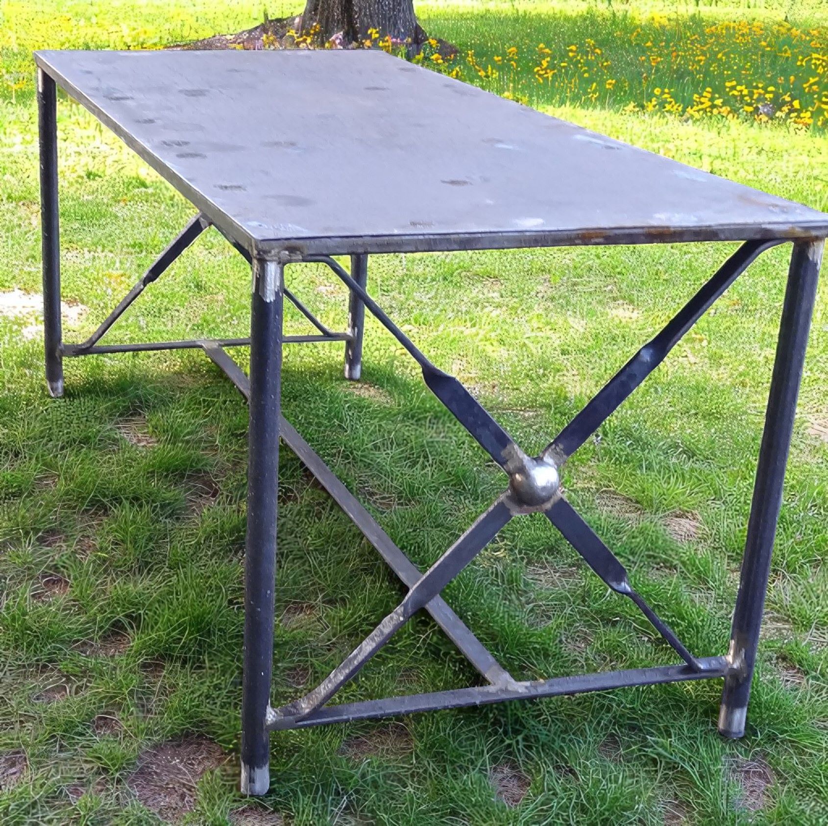 Table en métal avec un plateau gris foncé et des pieds noirs, sur une pelouse.