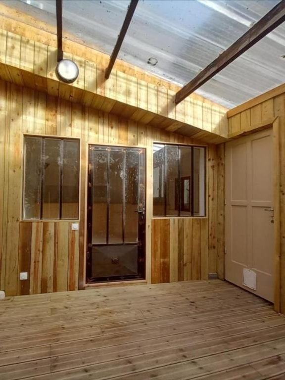 Pièce intérieure en bois avec fenêtres et porte ; murs et sol en planches de bois, toit transparent.