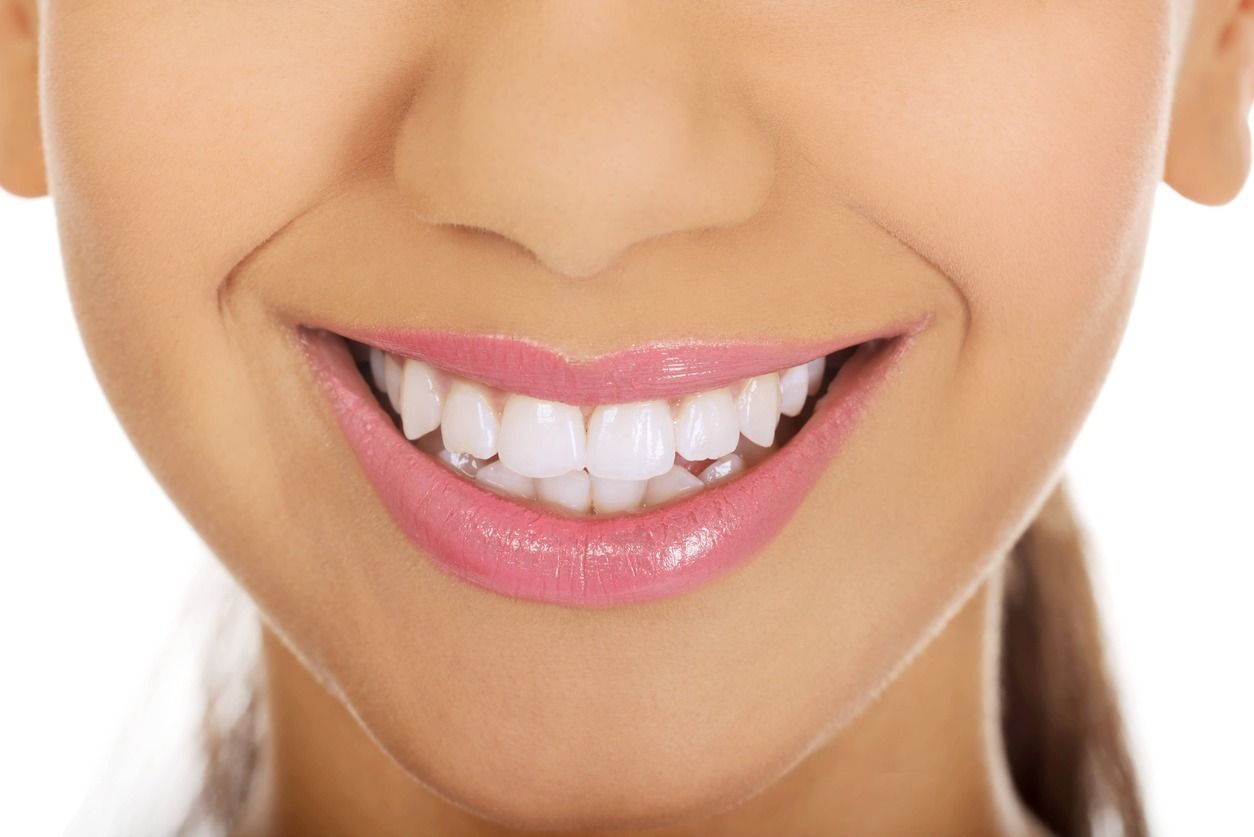 Un primer plano de la sonrisa de una mujer con dientes blancos y labios rosados.
