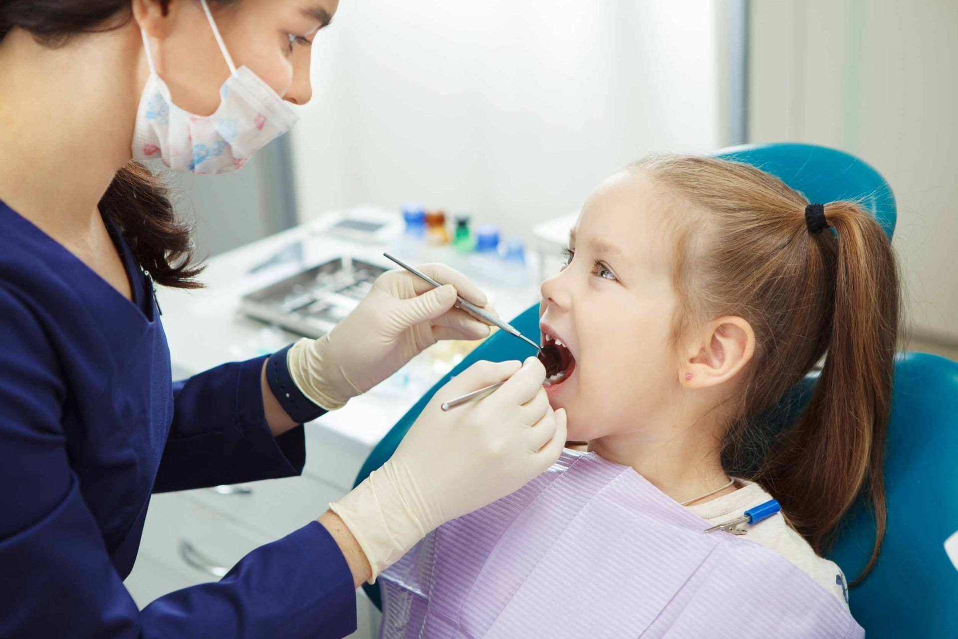 Una niña está sentada en una silla dental mientras un dentista le examina los dientes.