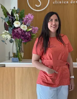 Una mujer está parada frente a un mostrador con un jarrón de flores encima.