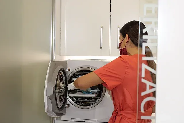 Una mujer está utilizando un autoclave en un consultorio dental.