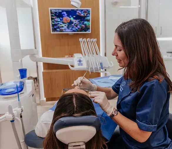 Una mujer está sentada en una silla dental mientras un dentista le examina los dientes.