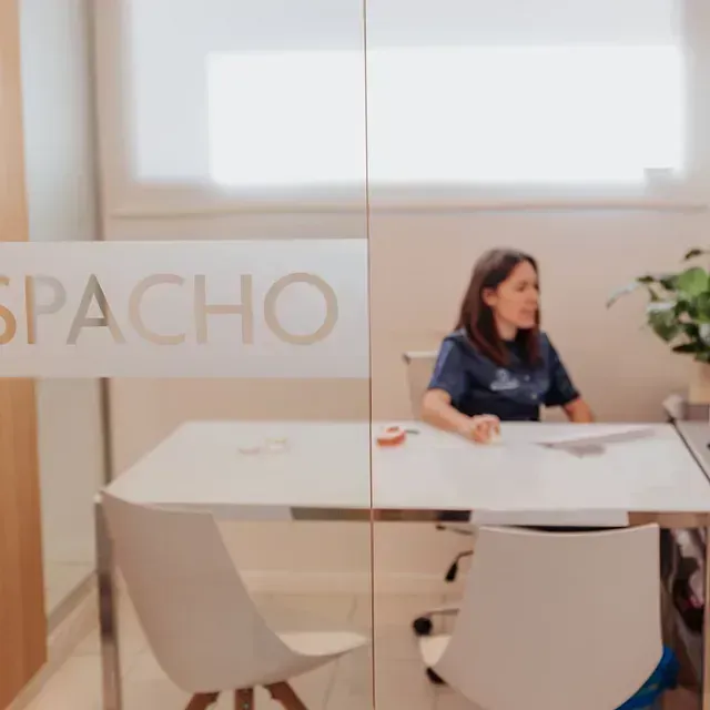Una mujer está sentada en una mesa frente a una pared de cristal.
