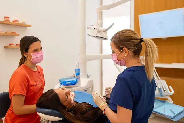 Dos dentistas examinan los dientes de una mujer en un consultorio dental.