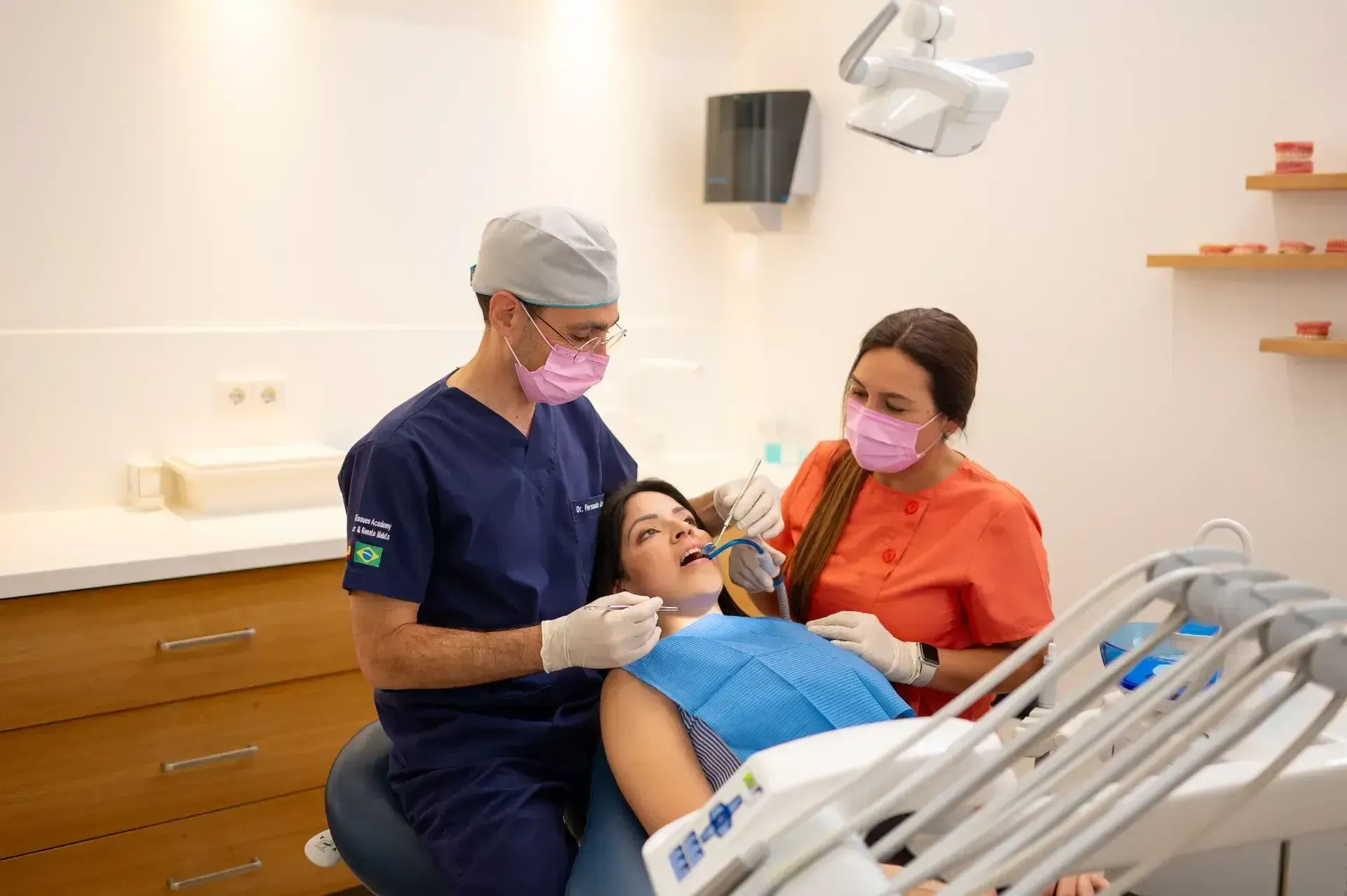 Una mujer está sentada en una silla dental mientras dos dentistas le examinan los dientes.