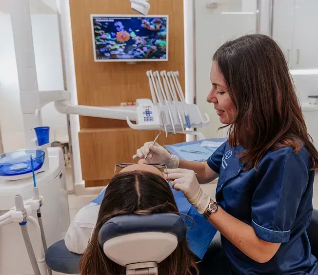 Una mujer está sentada en una silla dental mientras un dentista le examina los dientes.