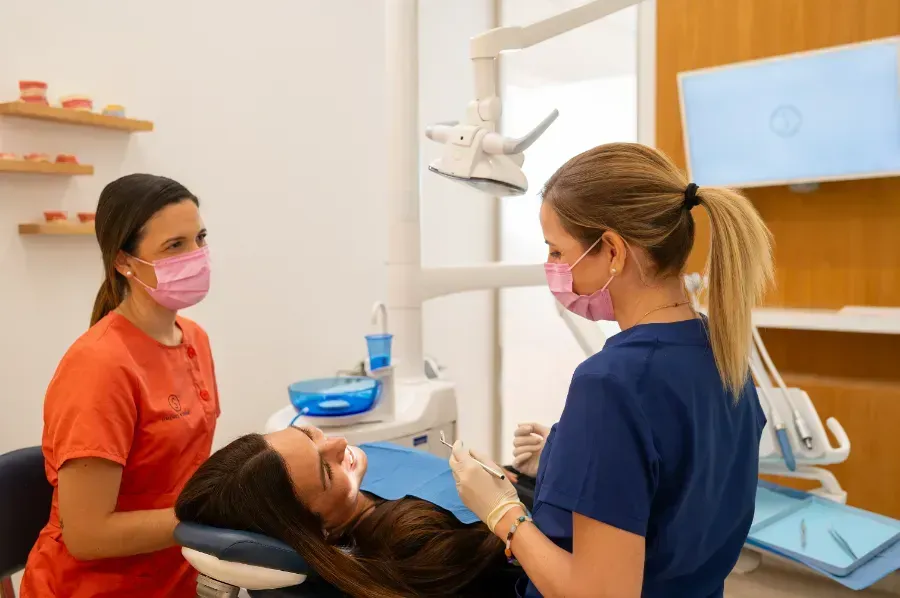 Una mujer está acostada en una silla dental mientras dos dentistas la observan.