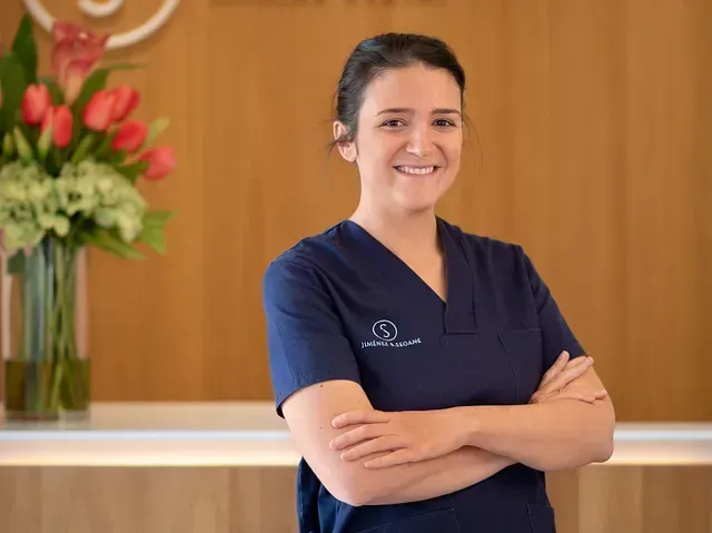 Una mujer con un uniforme azul está parada frente a un mostrador con los brazos cruzados.