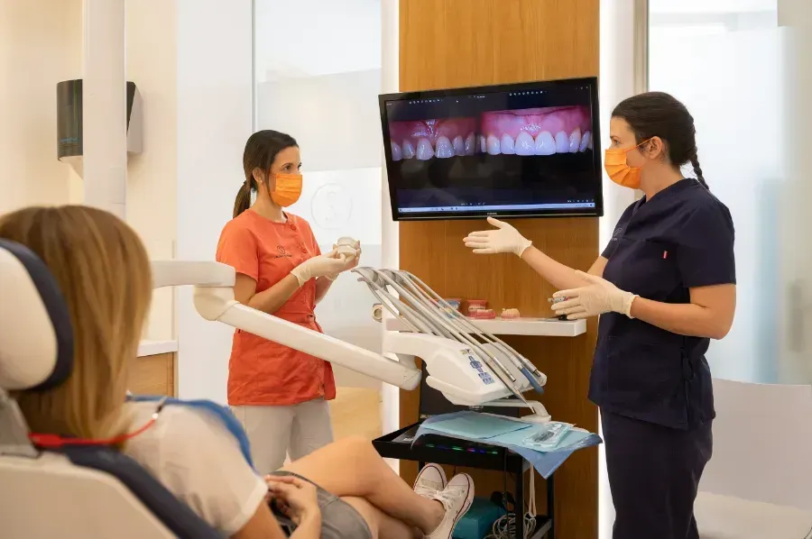 Dos dentistas mujeres están hablando con un paciente en una silla dental.