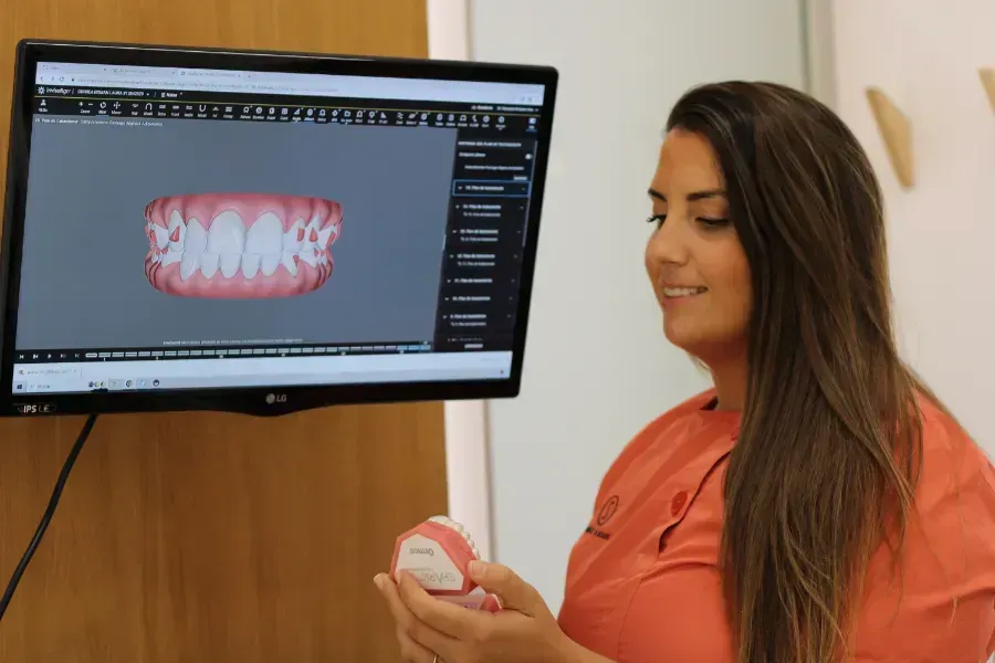Una mujer sostiene un modelo de sus dientes frente a una pantalla de computadora.