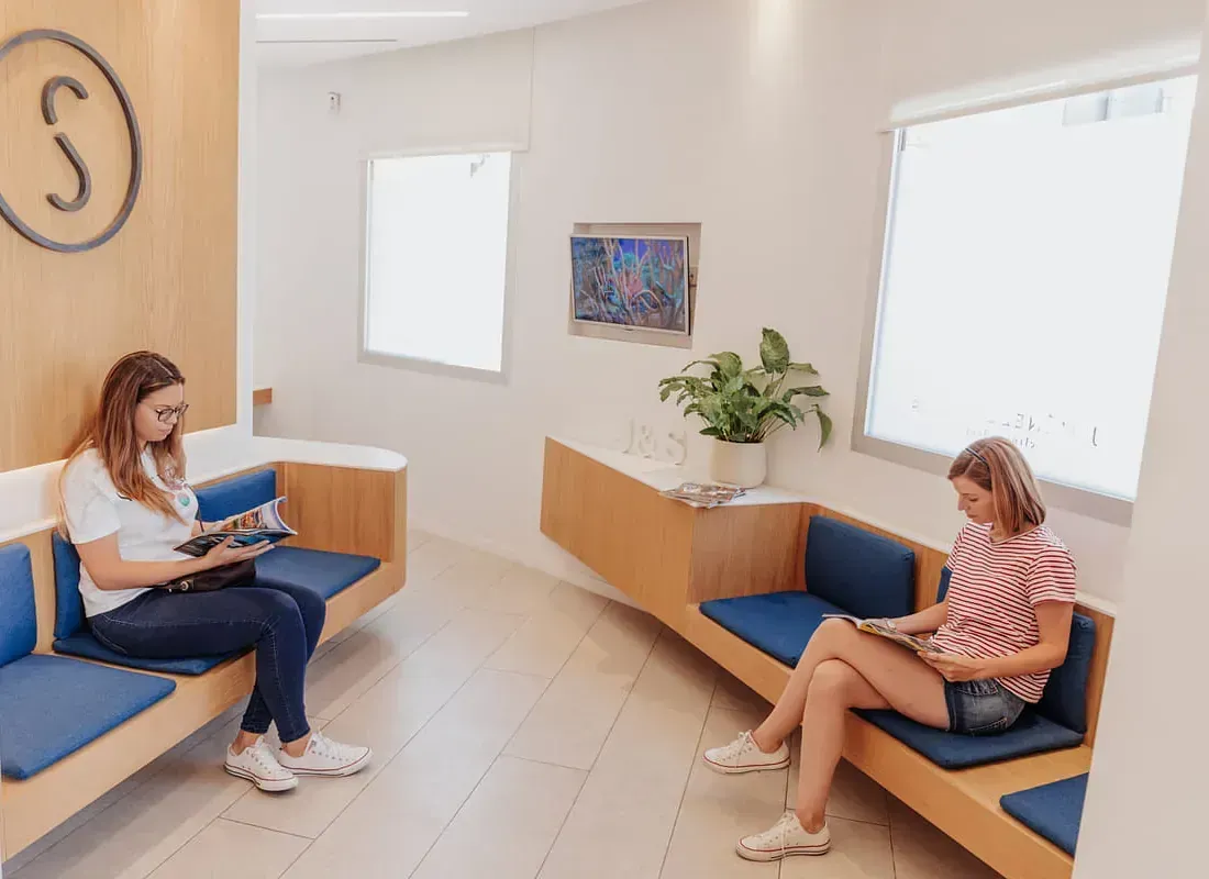 Dos mujeres están sentadas en una sala de espera en un consultorio dental.
