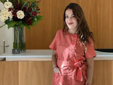 Una mujer está parada frente a un mostrador con un jarrón de flores en el fondo.