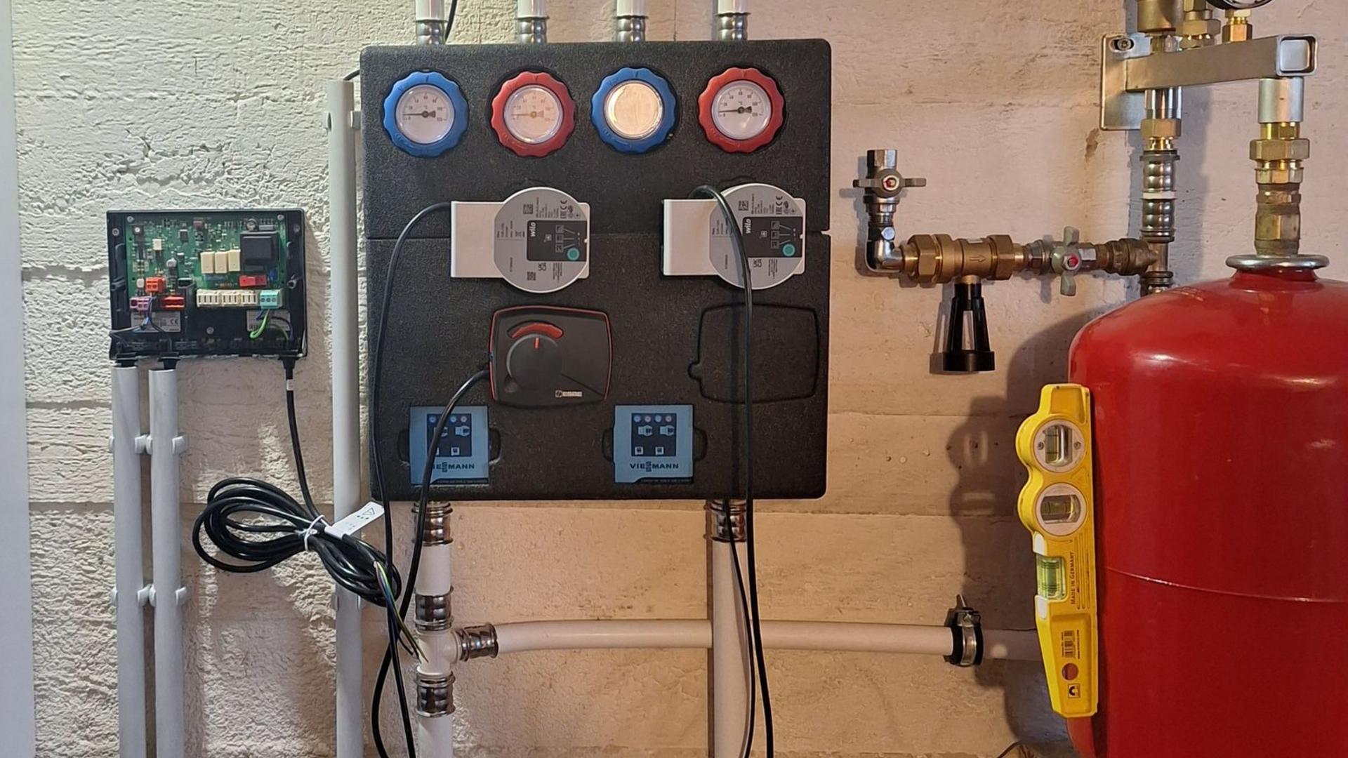 Panneau de commande mural avec jauges, écrans et équipements connectés, à côté d'un réservoir rouge.