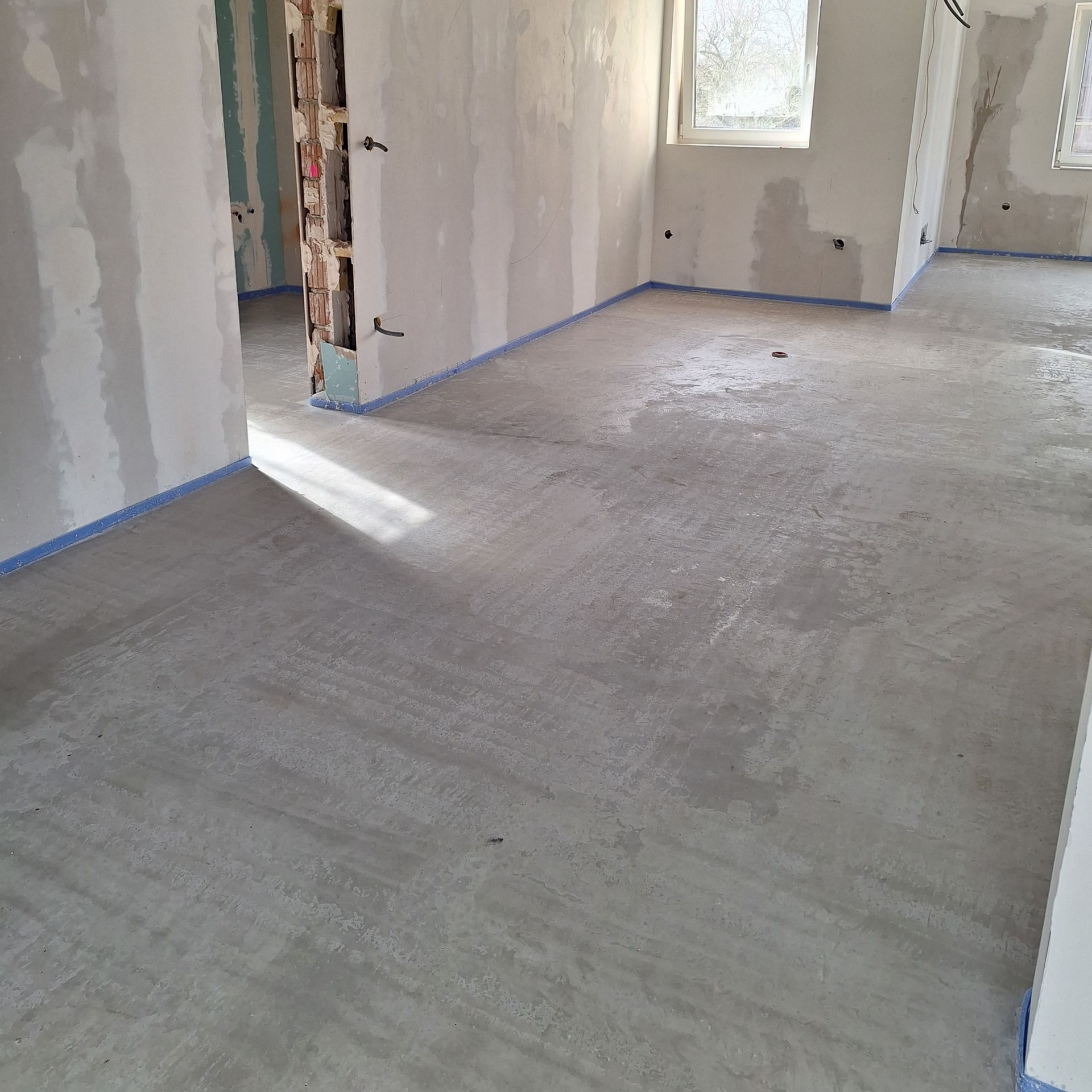 Sol en béton avec ruban adhésif bleu, travaux d'intérieur. Fenêtre en arrière-plan, murs enduits.