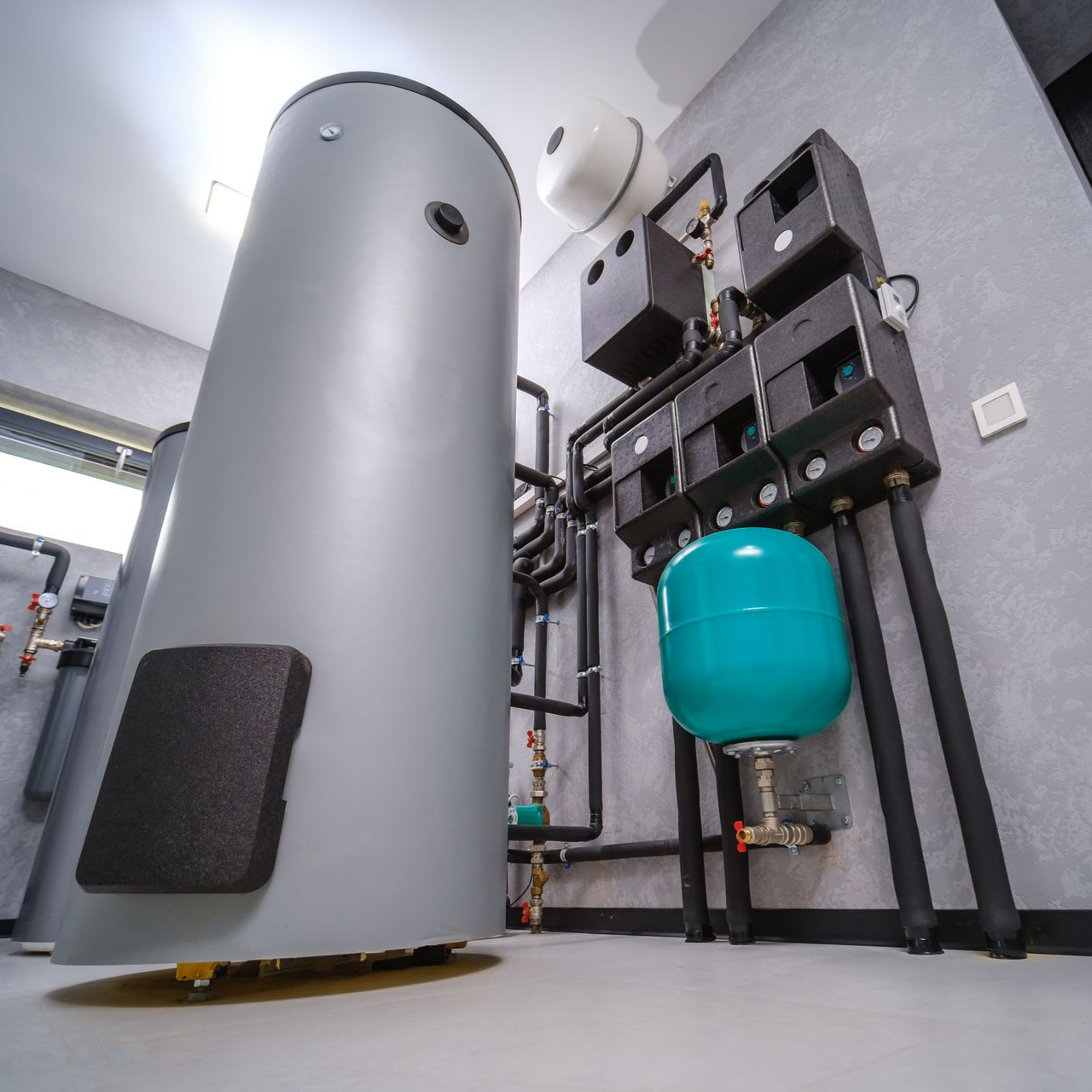 Grand réservoir d'eaux grises avec tuyauterie raccordée et vase d'expansion turquoise dans un local technique.