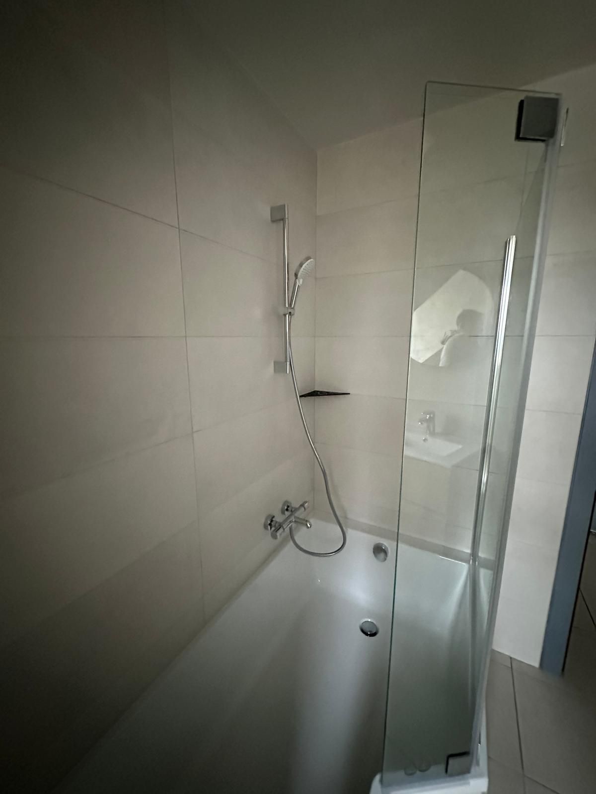 Salle de bains avec baignoire blanche, pommeau de douche et paroi de douche en verre contre un mur carrelé.