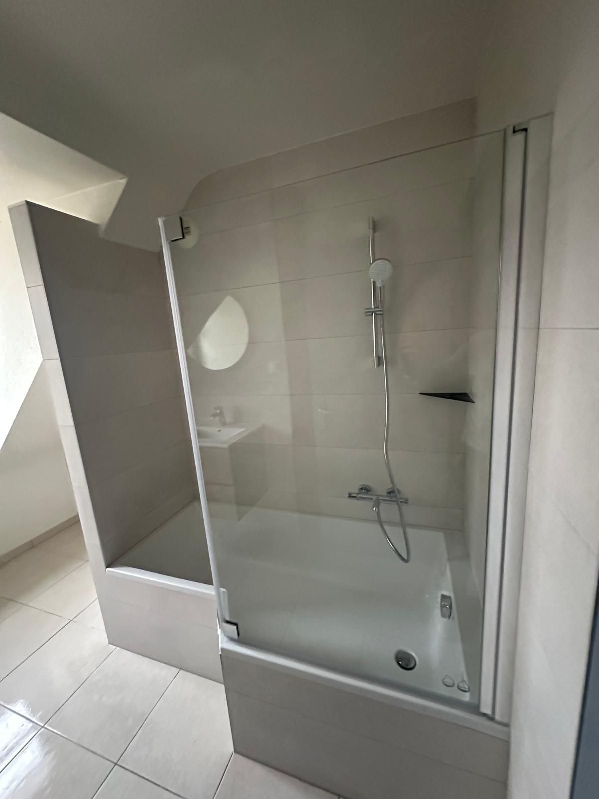 Salle de bains avec baignoire blanche, paroi de douche en verre et murs carrelés blancs.