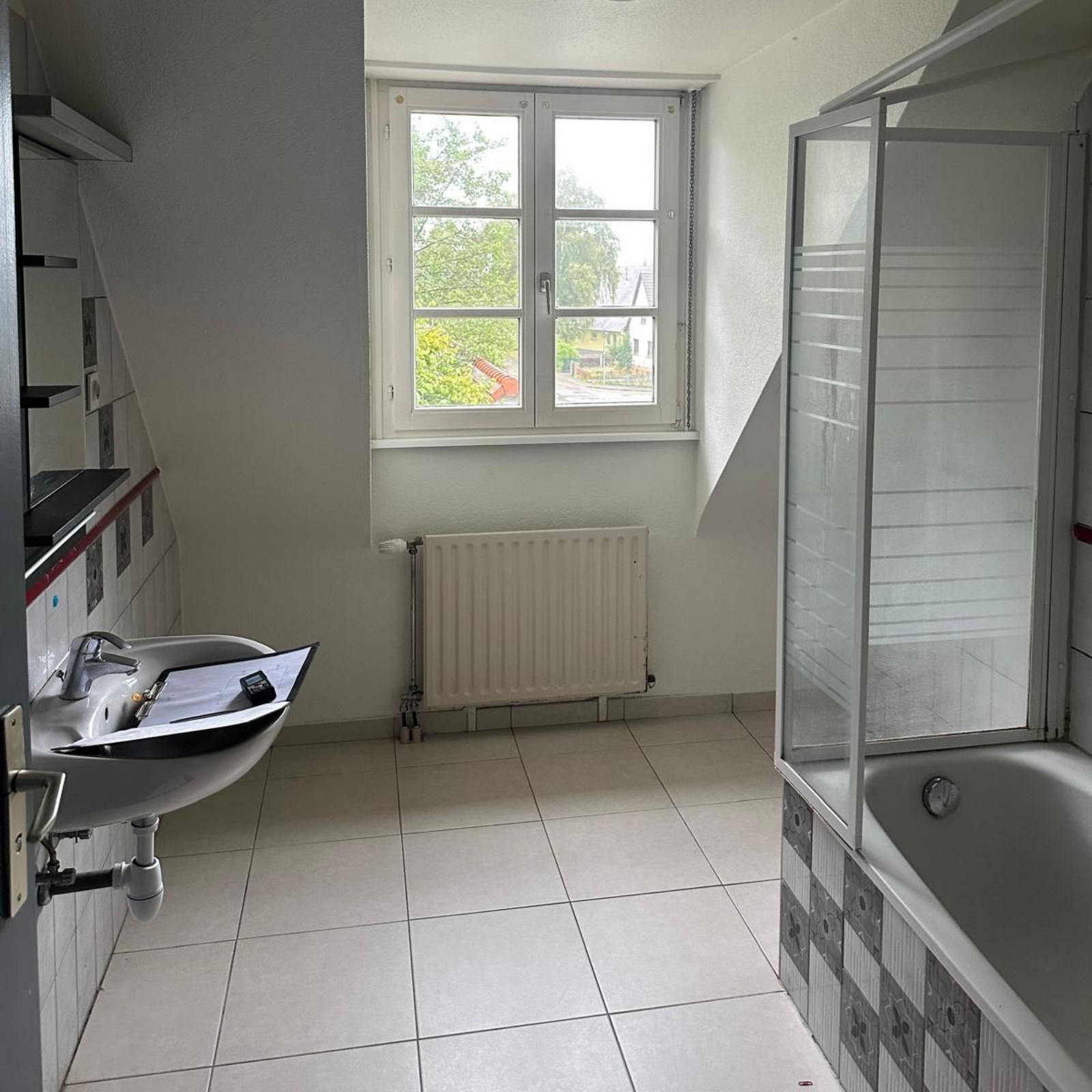 Salle de bains avec fenêtre, lavabo, baignoire et cabine de douche ; carrelage blanc et gris.