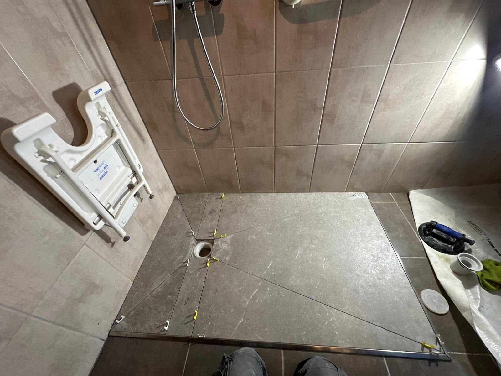 Cabine de douche avec murs et sol carrelés, bonde apparente. Siège rabattable fixé au mur.