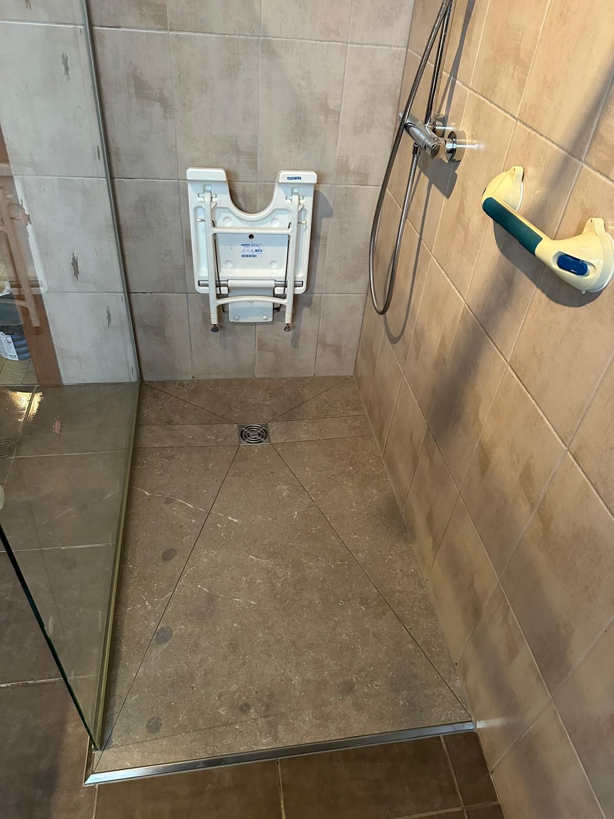 Douche avec siège rabattable et barre d'appui ; murs carrelés beiges.