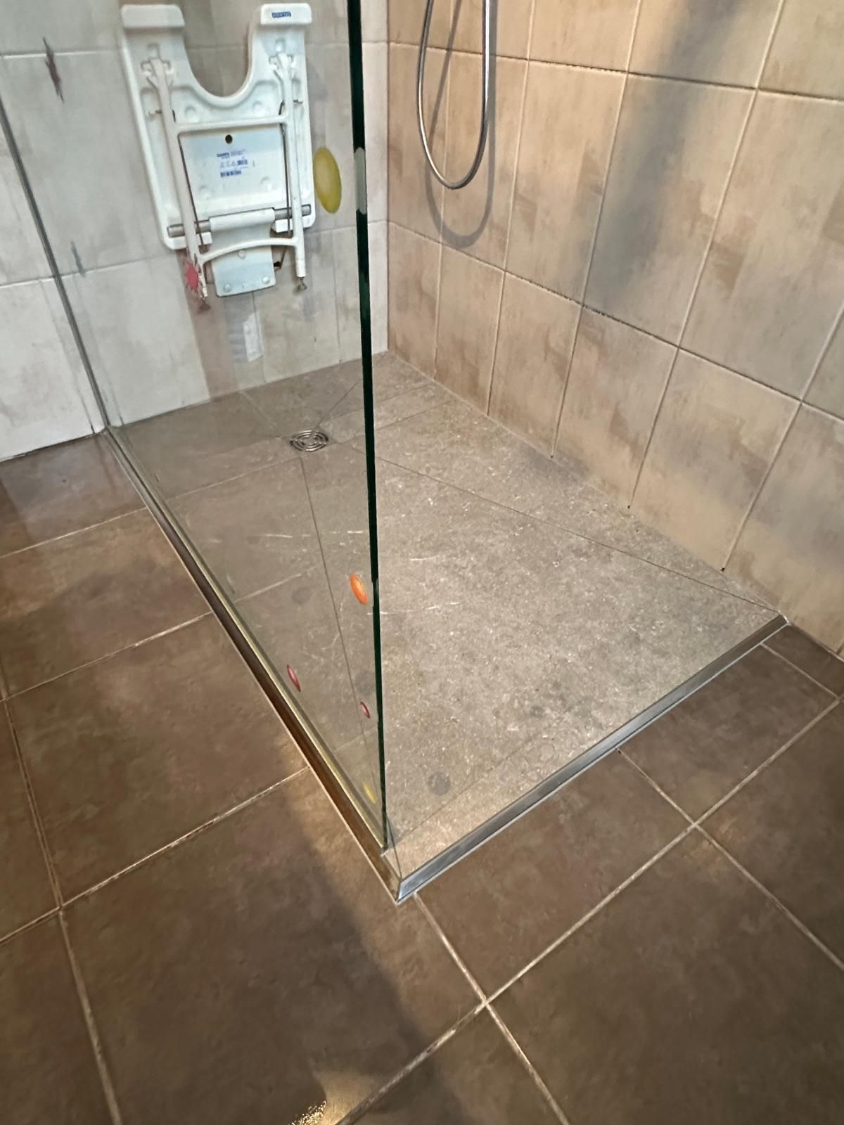 Douche avec porte en verre et sol carrelé gris.
