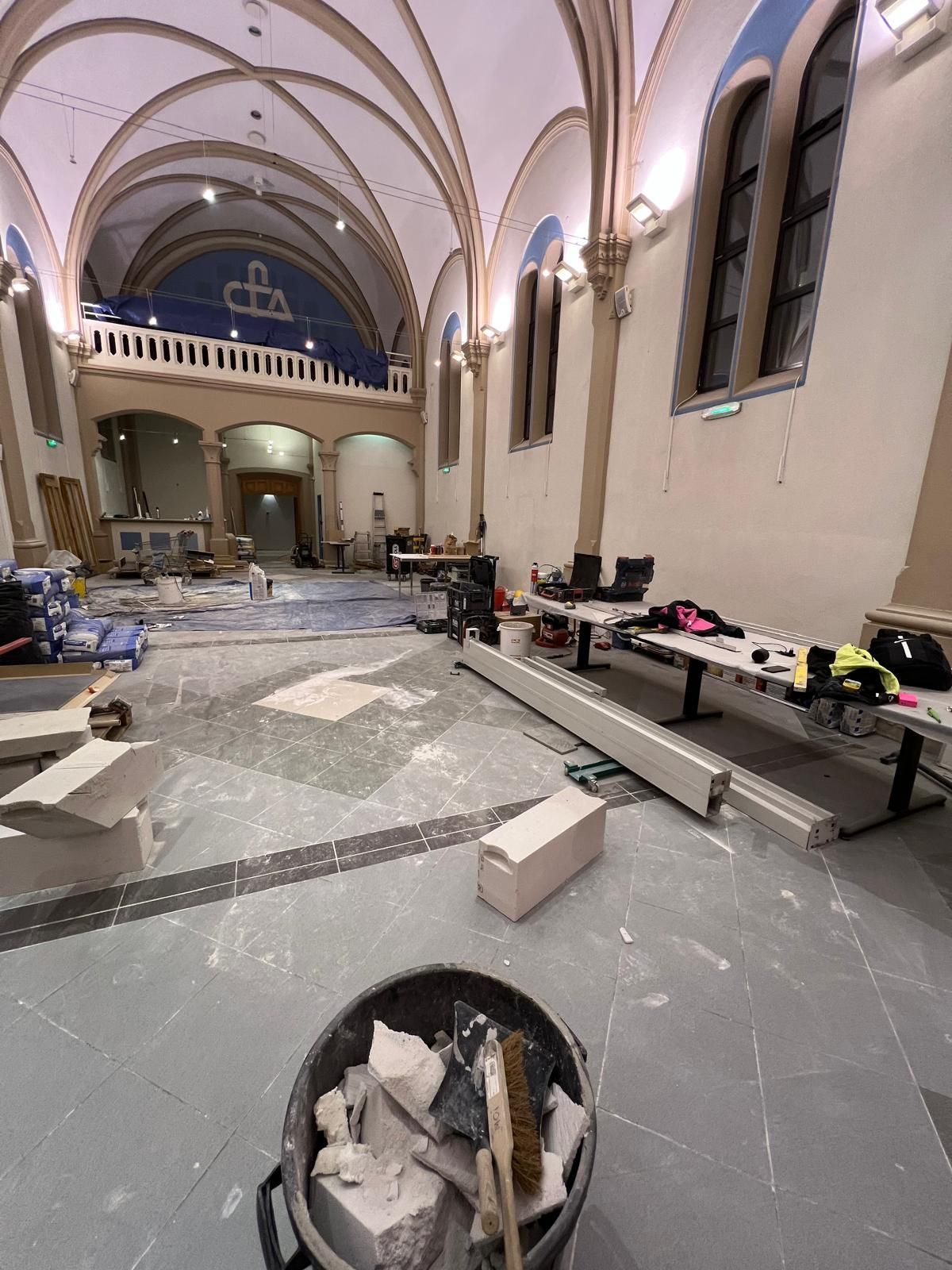 Vue intérieure d'une église en rénovation. Matériaux éparpillés au sol, échafaudages, haut plafond voûté.