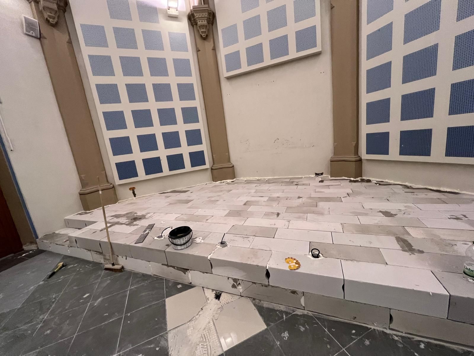 Pièce en construction, avec sol en parpaings et panneaux muraux à grille bleue.