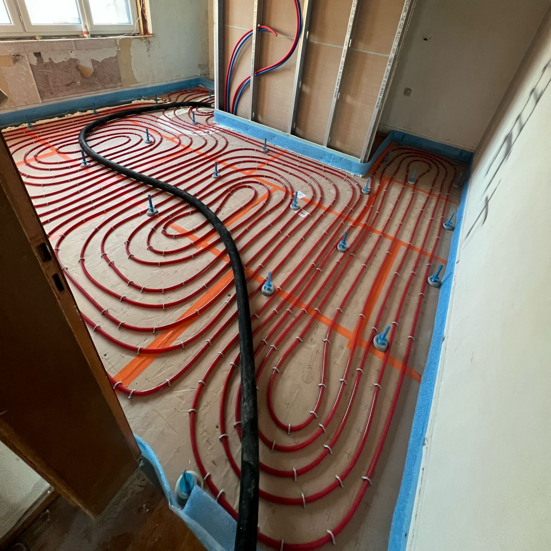 Tubes de chauffage au sol radiant rouges posés sur un sol, prêts à être installés, avec un tube central noir.