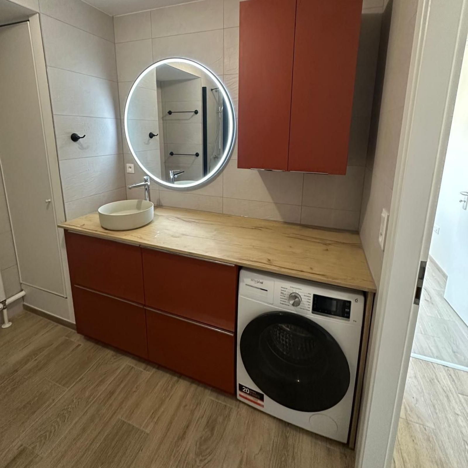 Salle de bains avec meubles rouges, miroir rond, lavabo et machine à laver.