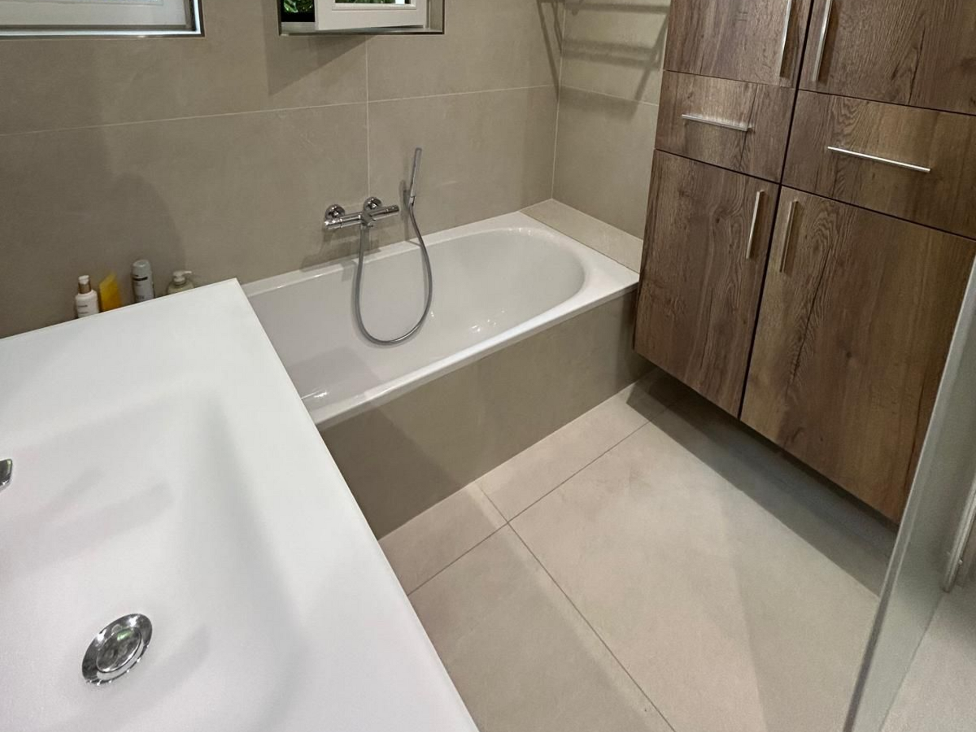 Salle de bains avec baignoire blanche, meuble-lavabo et armoires de rangement en bois.