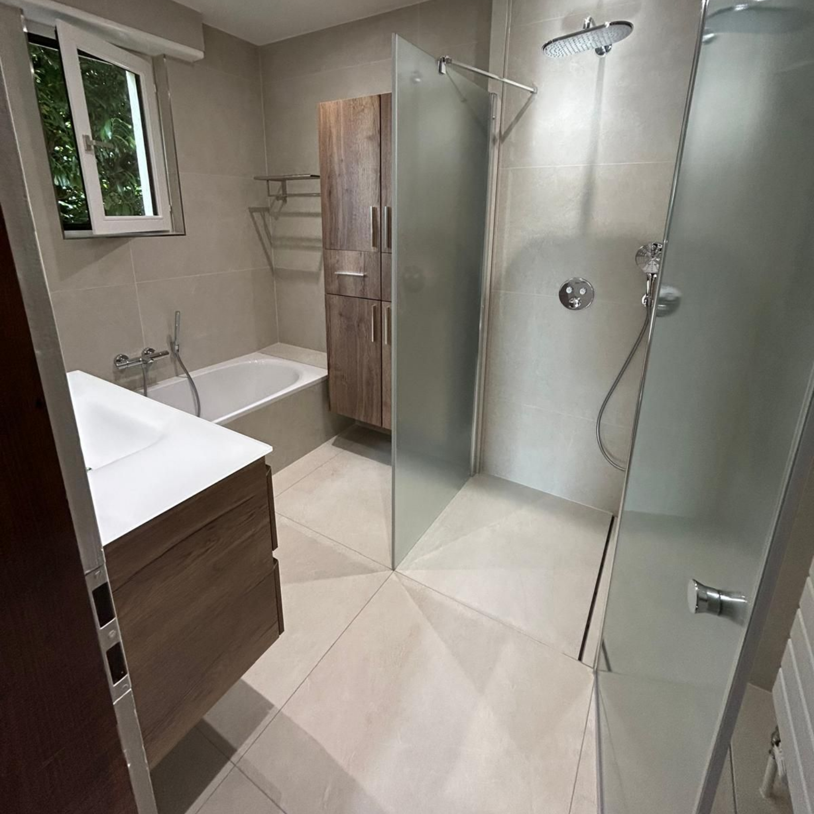 Salle de bains moderne avec douche, baignoire, meuble-lavabo et armoire de rangement en bois.