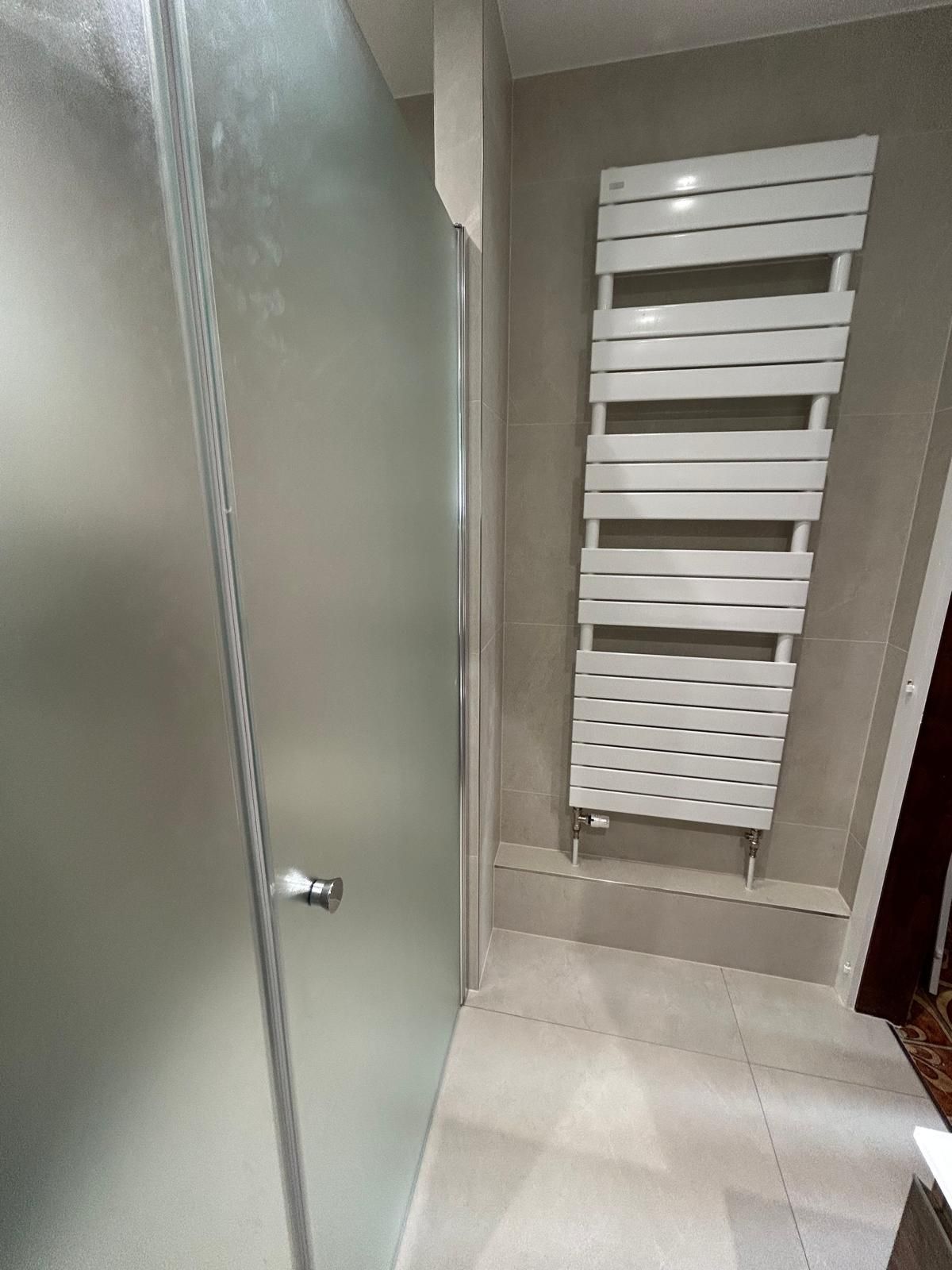 Douche avec porte en verre dépoli et sèche-serviettes blanc sur un mur carrelé gris clair.