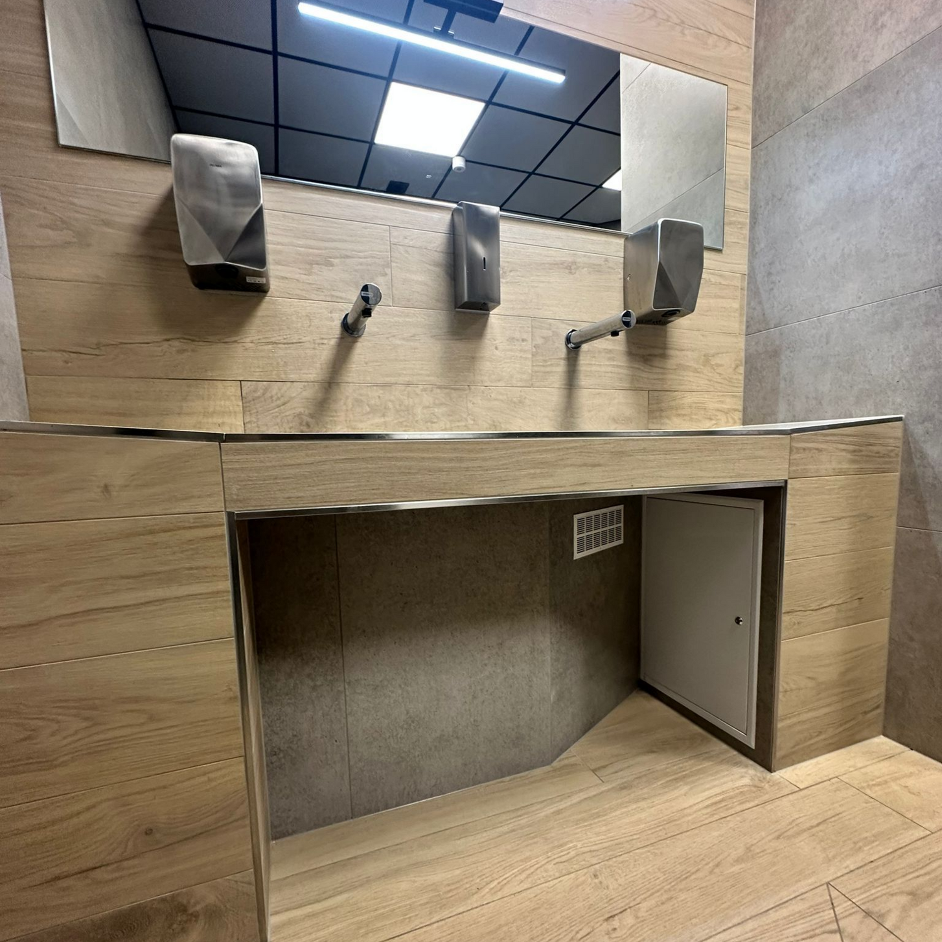 Toilettes modernes avec lavabos, miroir, distributeurs automatiques de savon et sèche-mains. Lambris et petite porte d'accès.