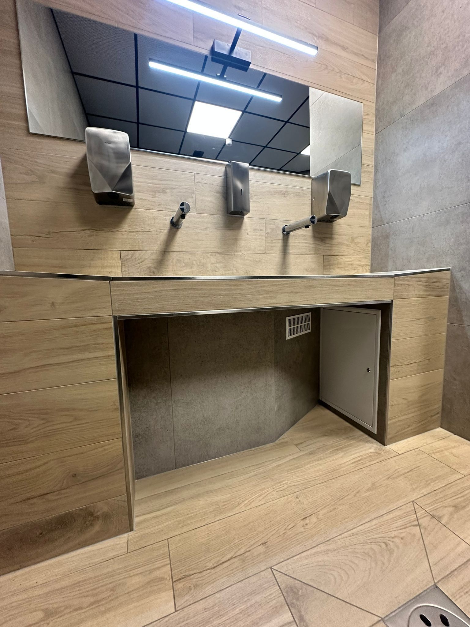 Espace lavabo moderne et accessible avec distributeurs, miroirs et espace ouvert pour le passage des fauteuils roulants.