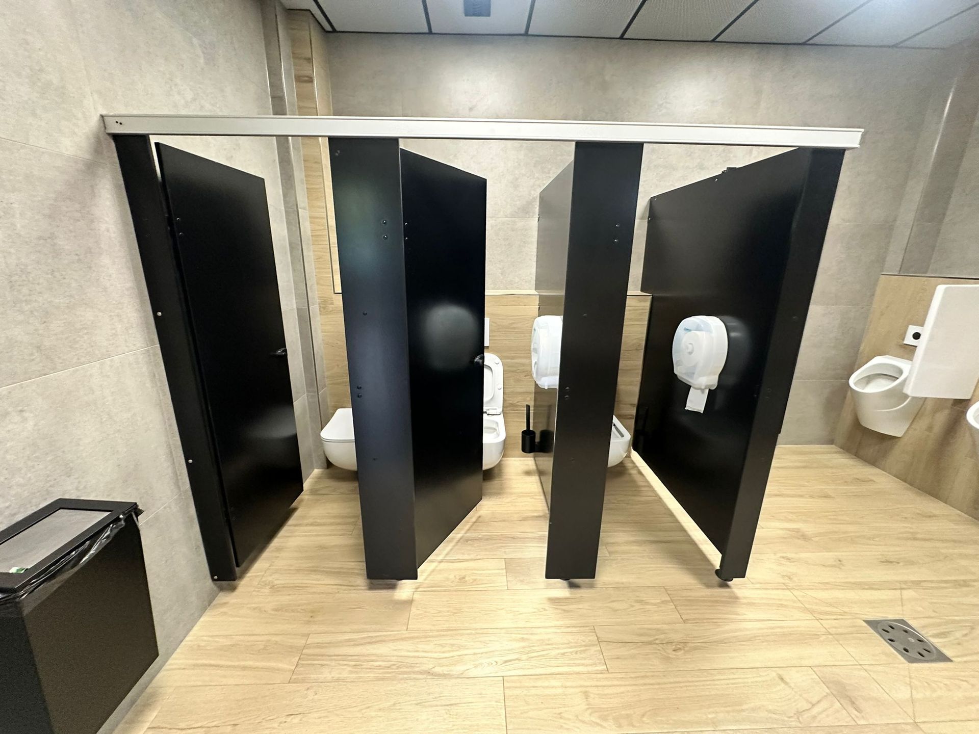 Toilettes publiques avec portes de cabine noires et murs et sol beiges.