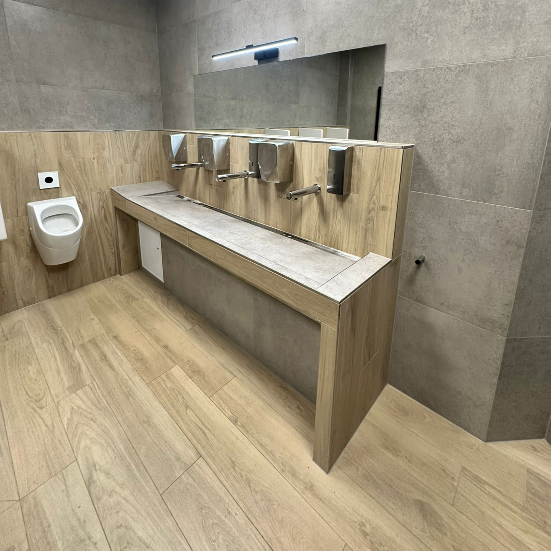 Toilettes publiques avec lavabos, distributeurs de savon et WC. Intérieur en bois et carrelage gris.