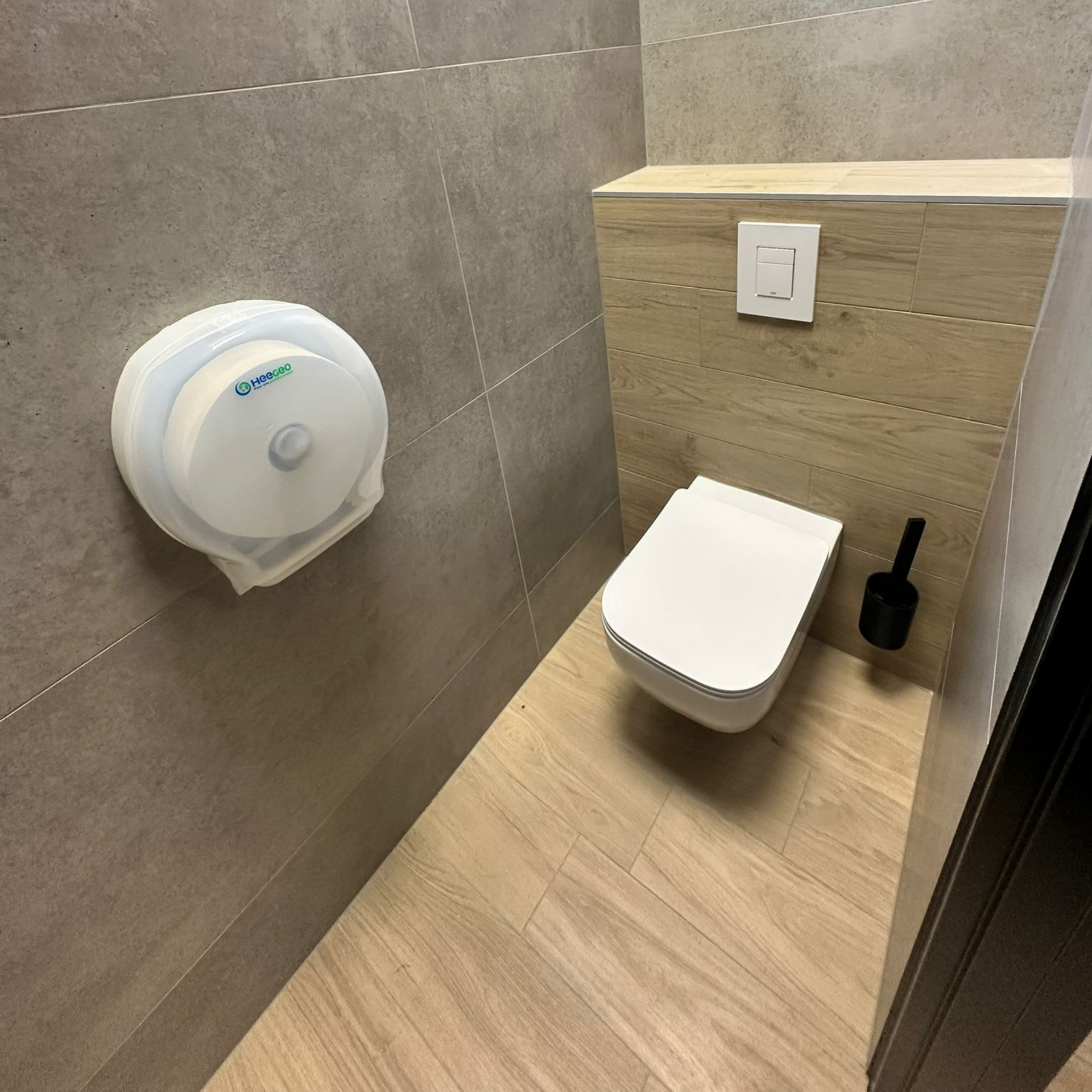Une petite salle de bains avec toilettes, distributeur de papier essuie-mains et brosse. Les murs sont carrelés et en bois.